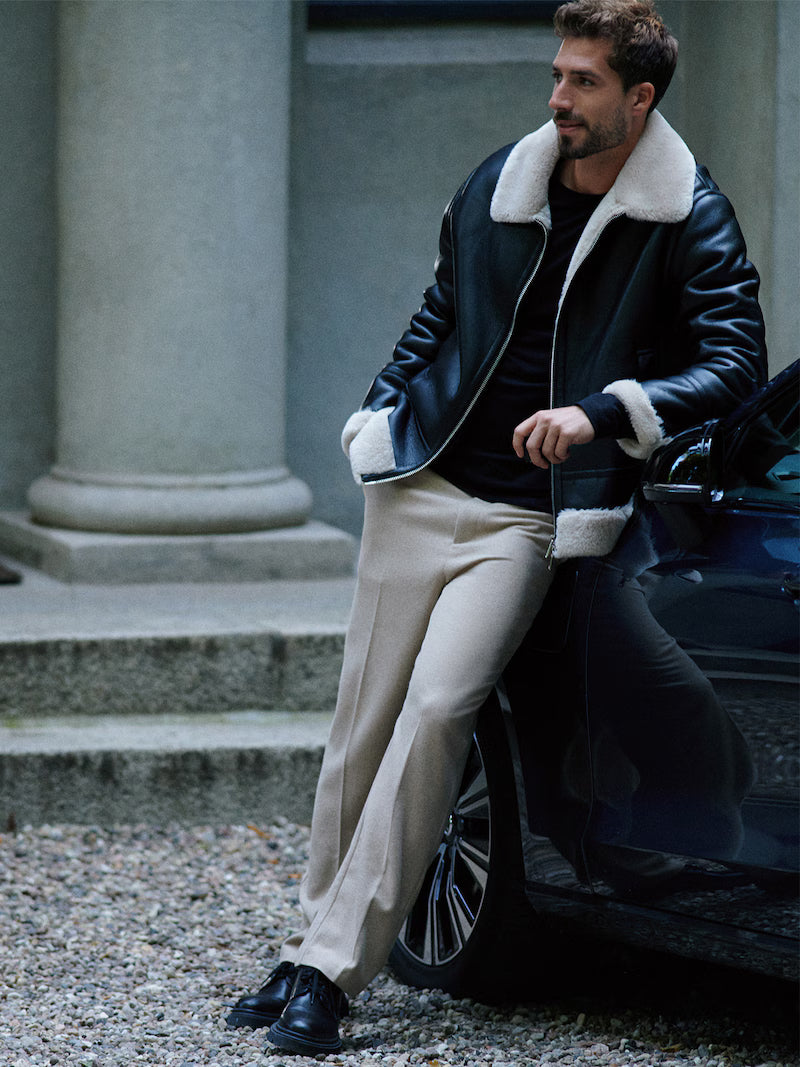 Man in a stylish outfit sitting next to a car in an urban setting